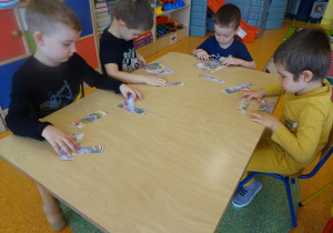 Czterech chłopców siedzi przy stole i składa z części obrazek łąki.